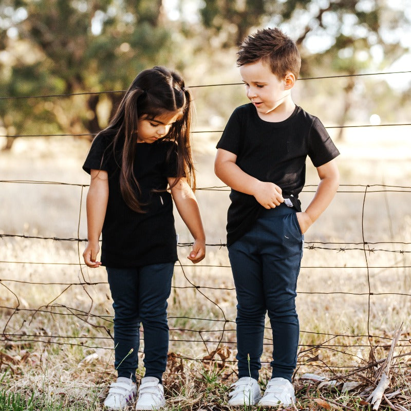 a boy and girl standing next to each other both wearing navy rye pants and black t-shirts